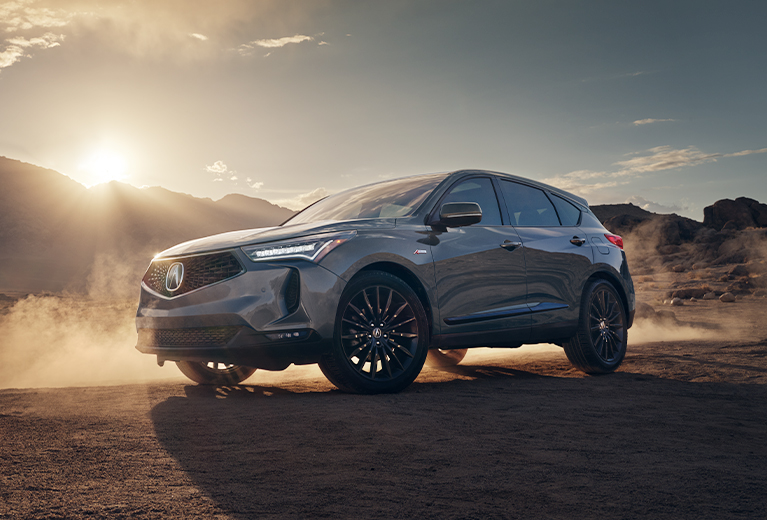 2022 Acura RDX A Spec in Liquid Carbon Metallic front in the desert kicking up dust at sunset (Premium Sport Crossover SUV).